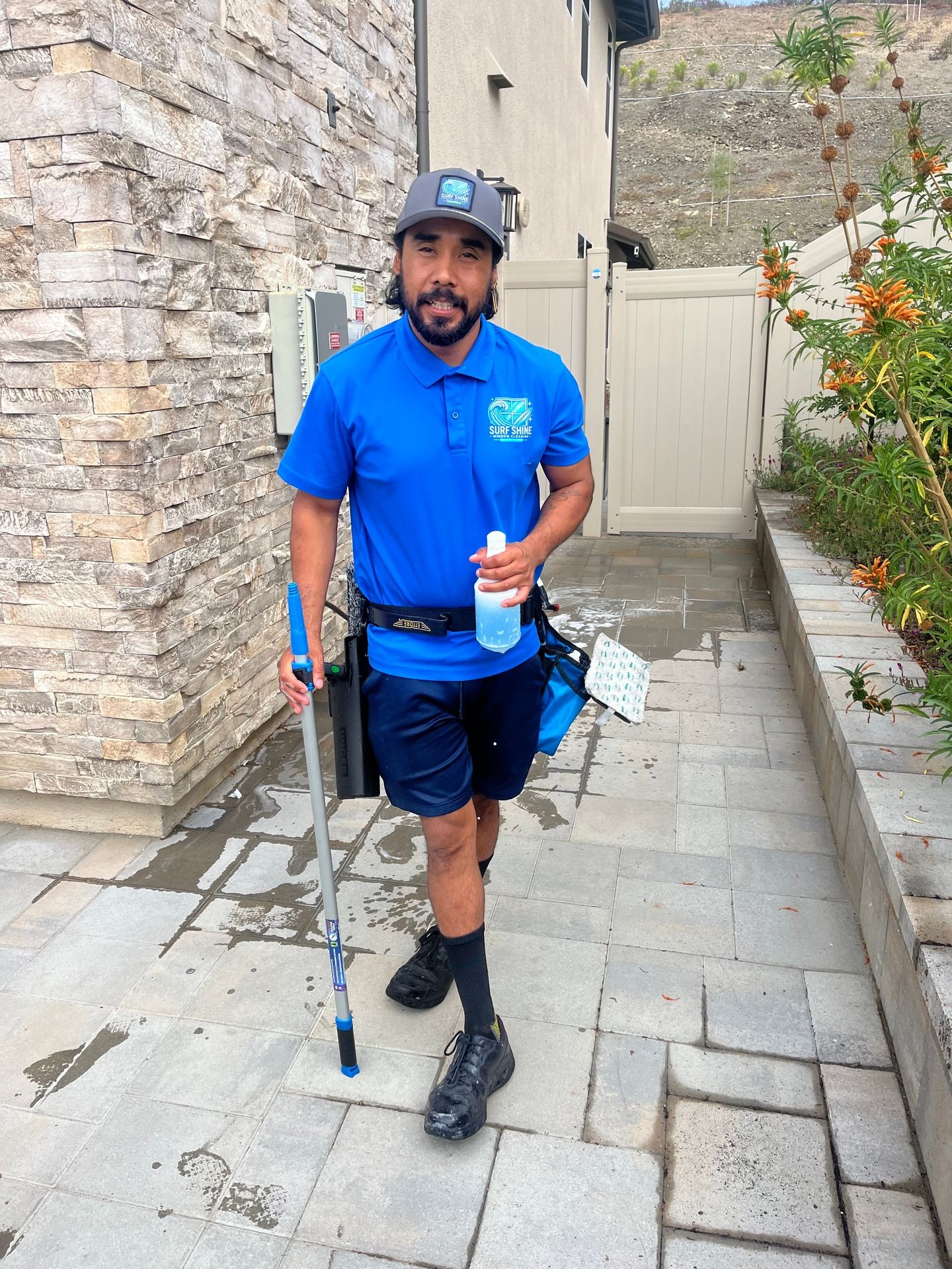 Man in blue uniform cleaning outdoor area with broom and cleaning supplies.